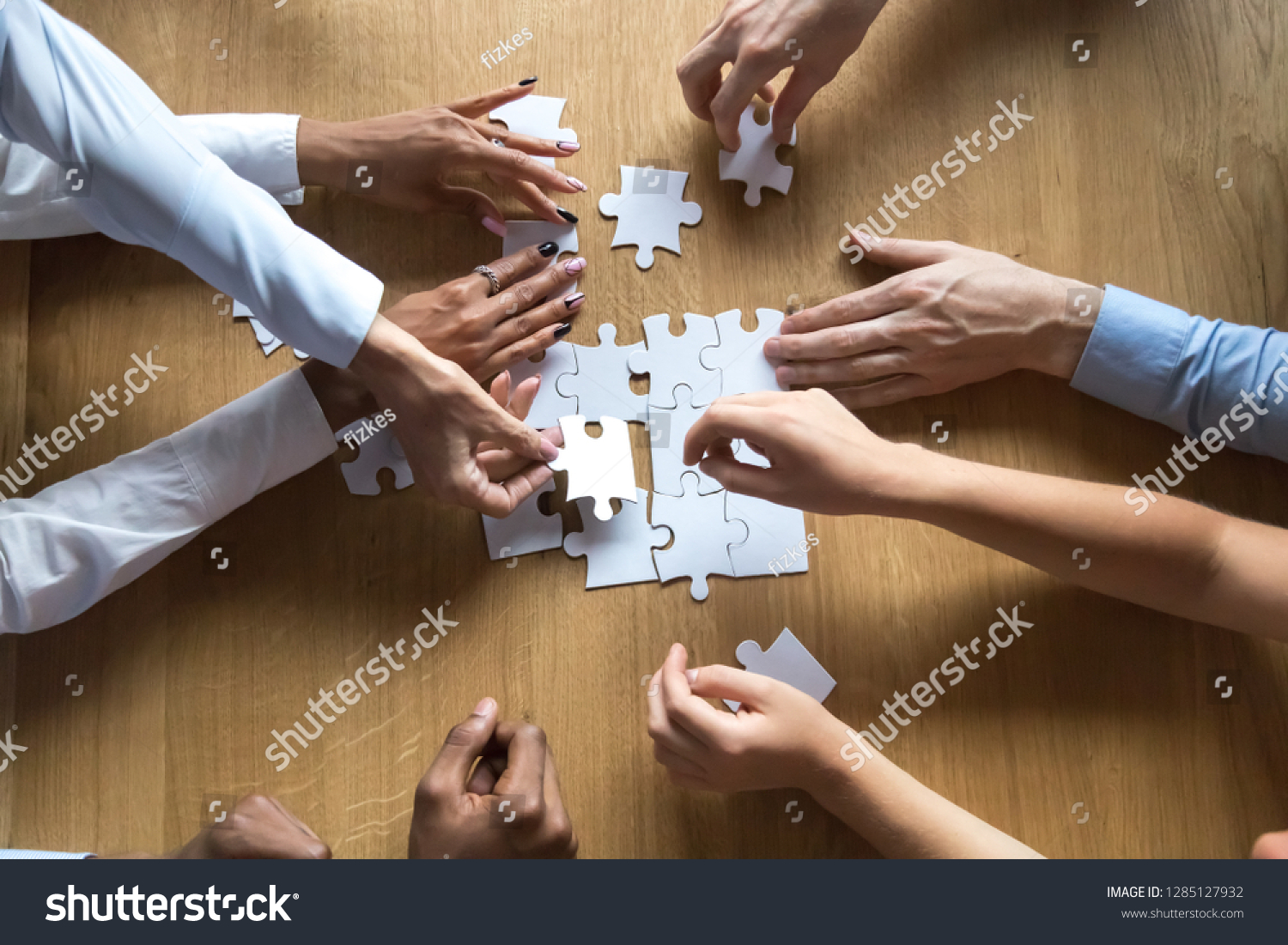 Above top view to the hands of diverse people assembling connecting jigsaw puzzle associates put pieces searching common solutions making right decisions together. Support and help in business concept #1285127932