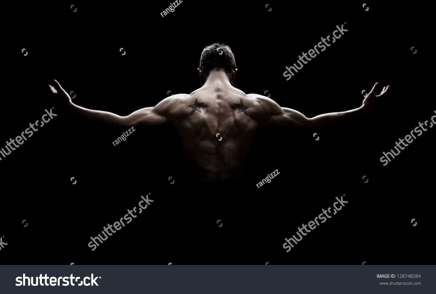 Rear view of healthy muscular young man with his arms stretched out isolated on black background #128748284