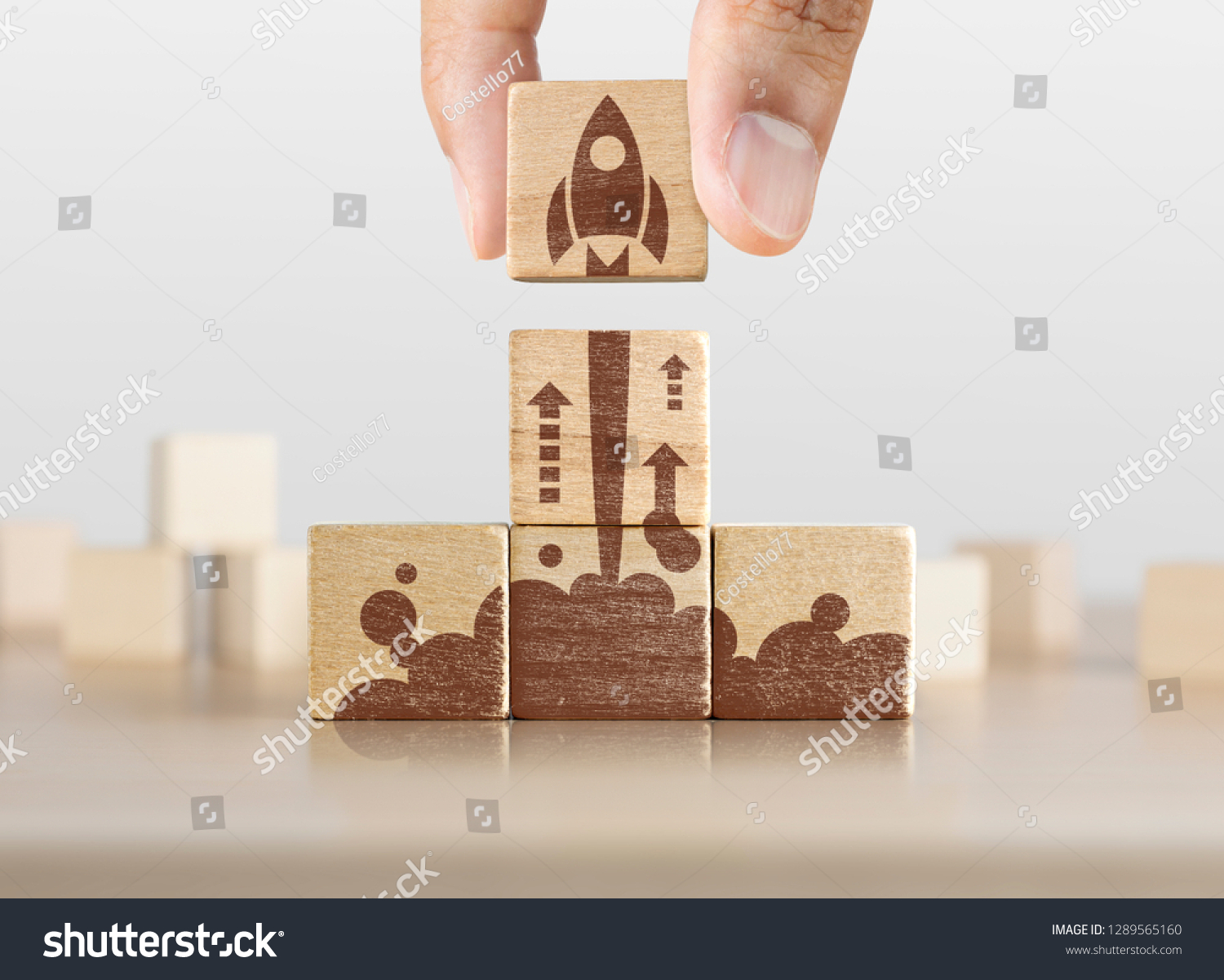 Business start up, start, new project or new idea concept. Wooden blocks with launching rocket graphic arranged in pyramid shape and a man is holding the top one. #1289565160