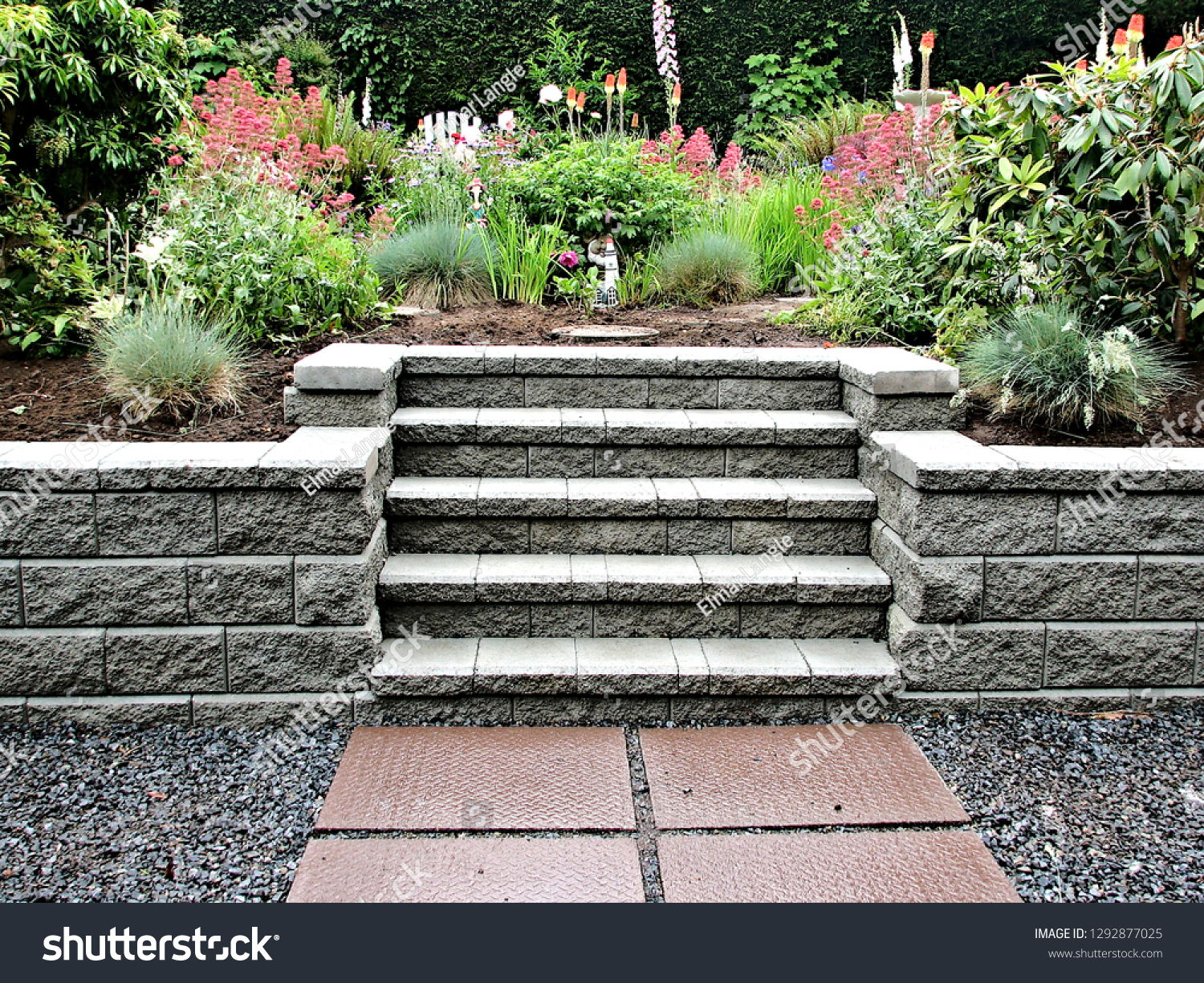 A beautiful block retaining wall in gray color with integrated staircase into existing garden landscaped with perennial flowers and shrubs  #1292877025