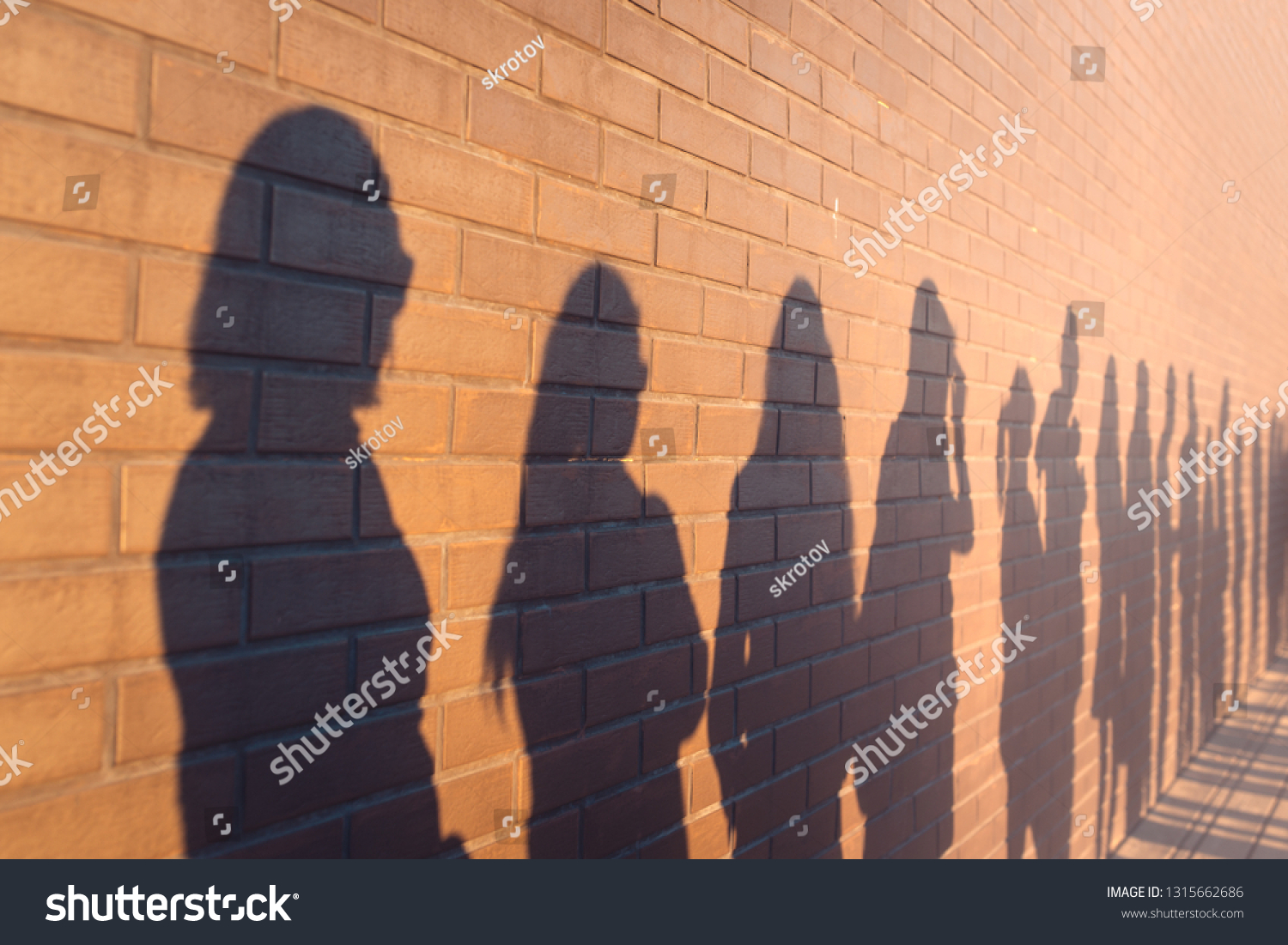 a line of shadows of people lined up against a red brick wall. Stand in a queue to the changes #1315662686