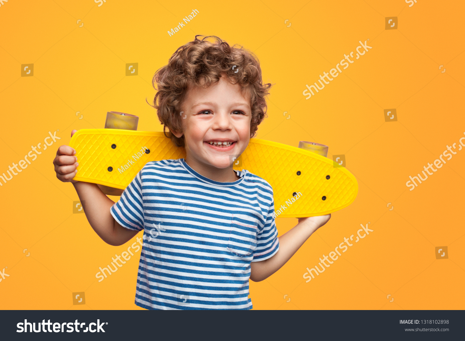 Happy little kid in striped t-shirt holding yellow longboard and smiling away on orange background #1318102898