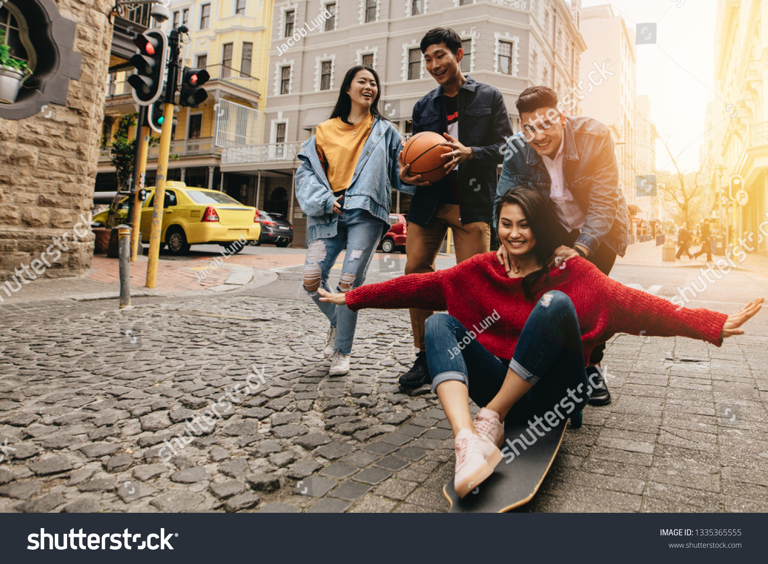 Asian young people in the city with skateboard and basketball. Woman being pushed by man  on skateboard outdoors on street, with their friends walking by in the city street. #1335365555