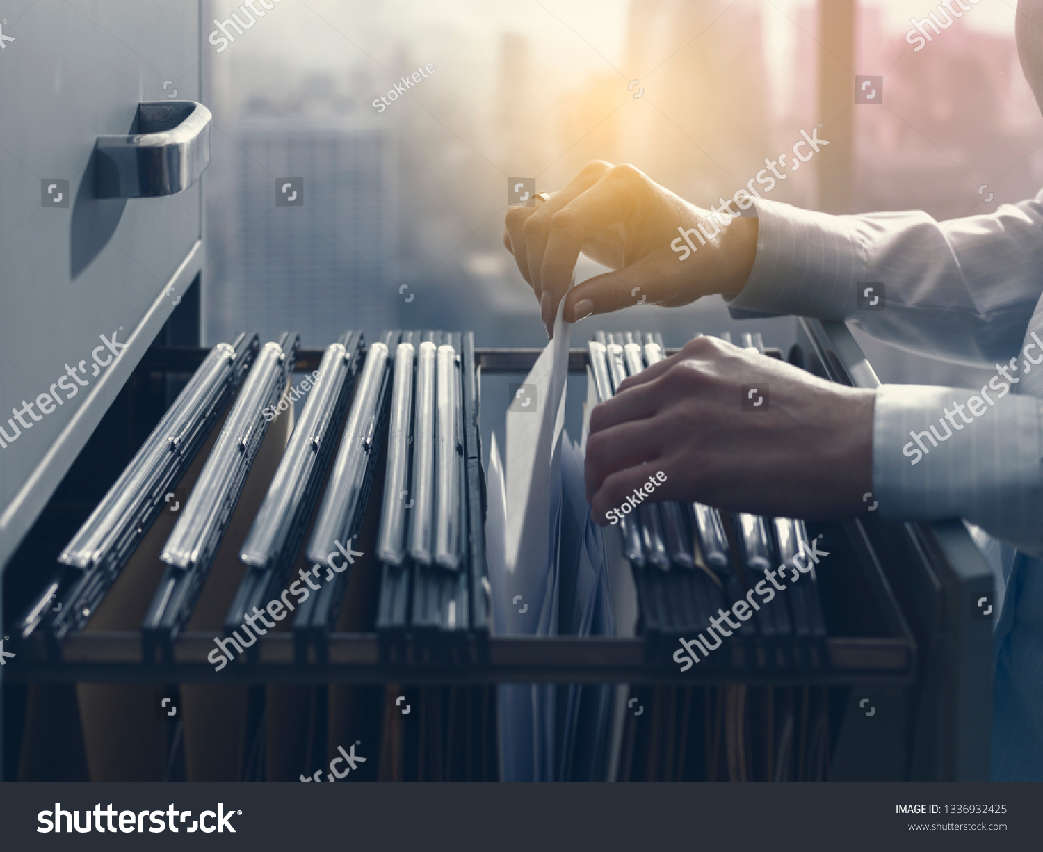 Professional female office clerk searching files and paperwork in the filing cabinet #1336932425