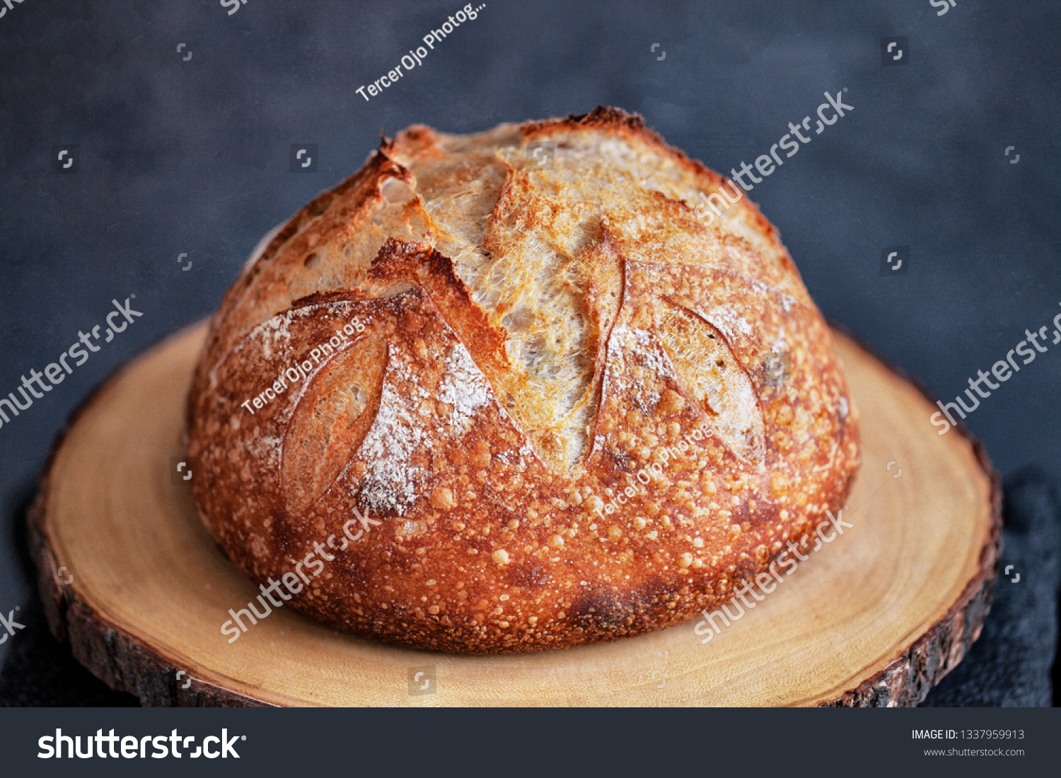 Round loaf of freshly baked homemade artisan sourdough bread on a round wood plank #1337959913