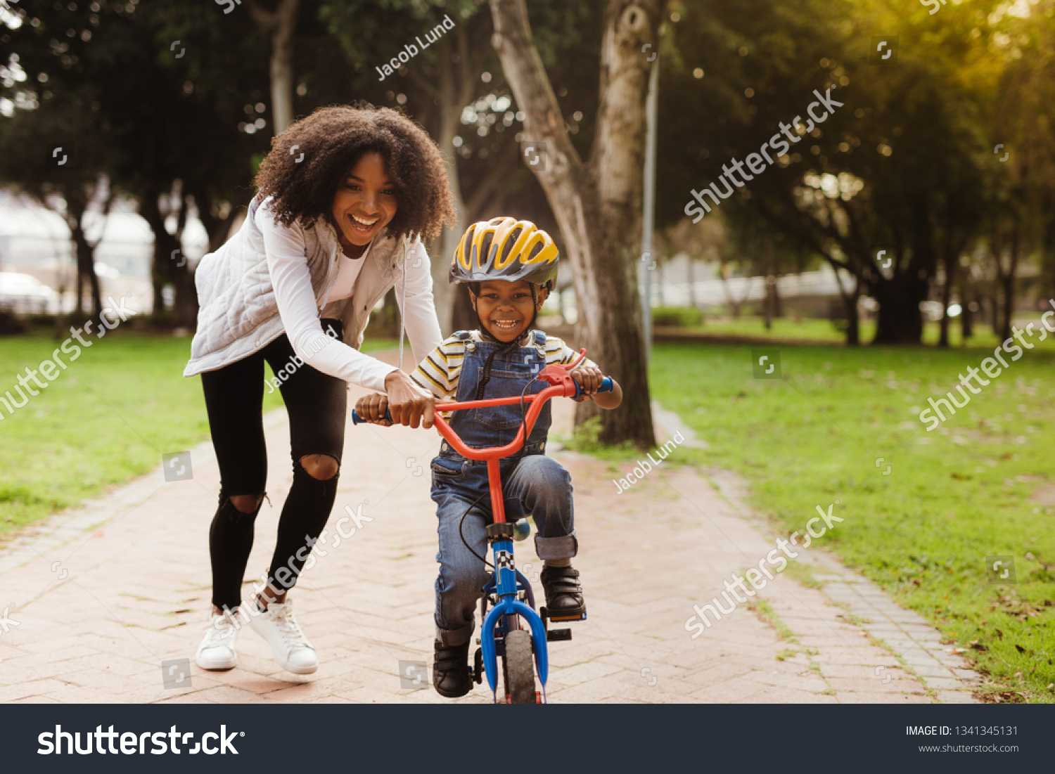 Happy cute boy learn to ride a bike with his mother. Mother teaching son to ride bicycle at park. #1341345131