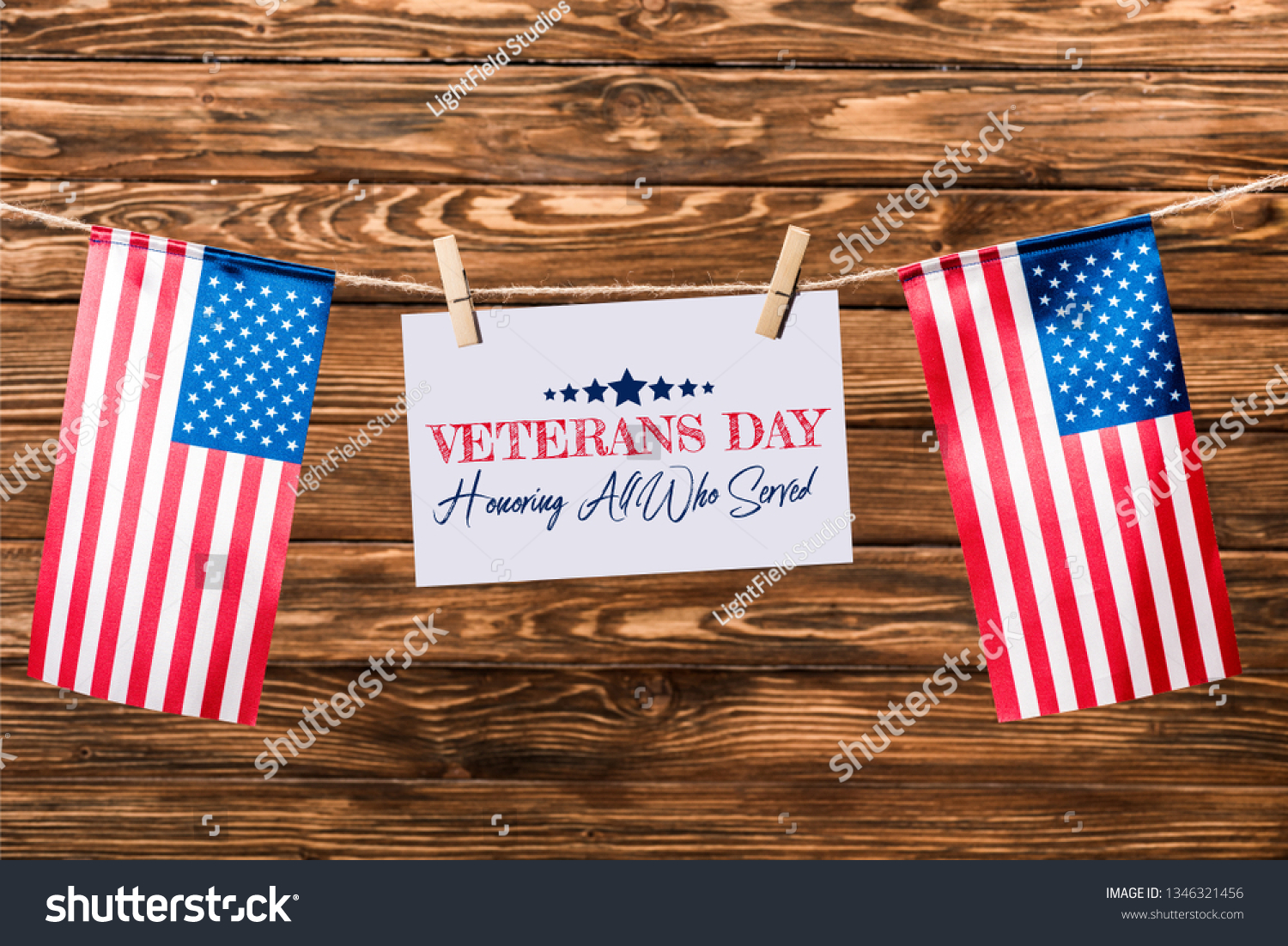 card with veterans day lettering hanging on string with pins and american flags on wooden background #1346321456