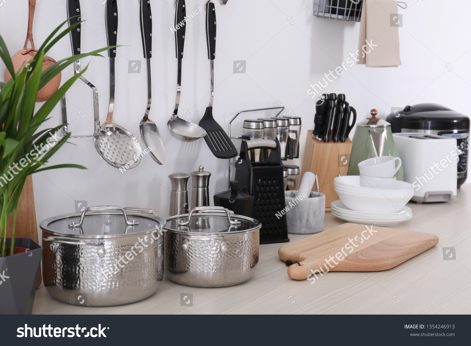 Set of clean cookware, dishes, utensils and appliances on table at white wall #1354246913