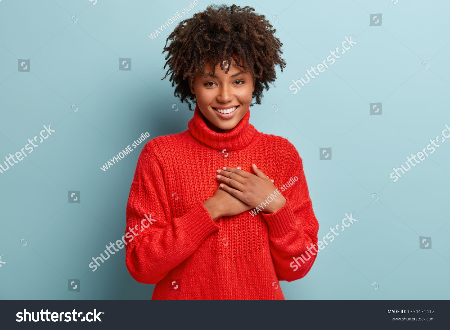 Photo of emotional dark skinned female touches heart with both palms, demonstrates thankful gesture, has good natured expression, expresses great sympathy, gratitude with honesty, feels love #1354471412