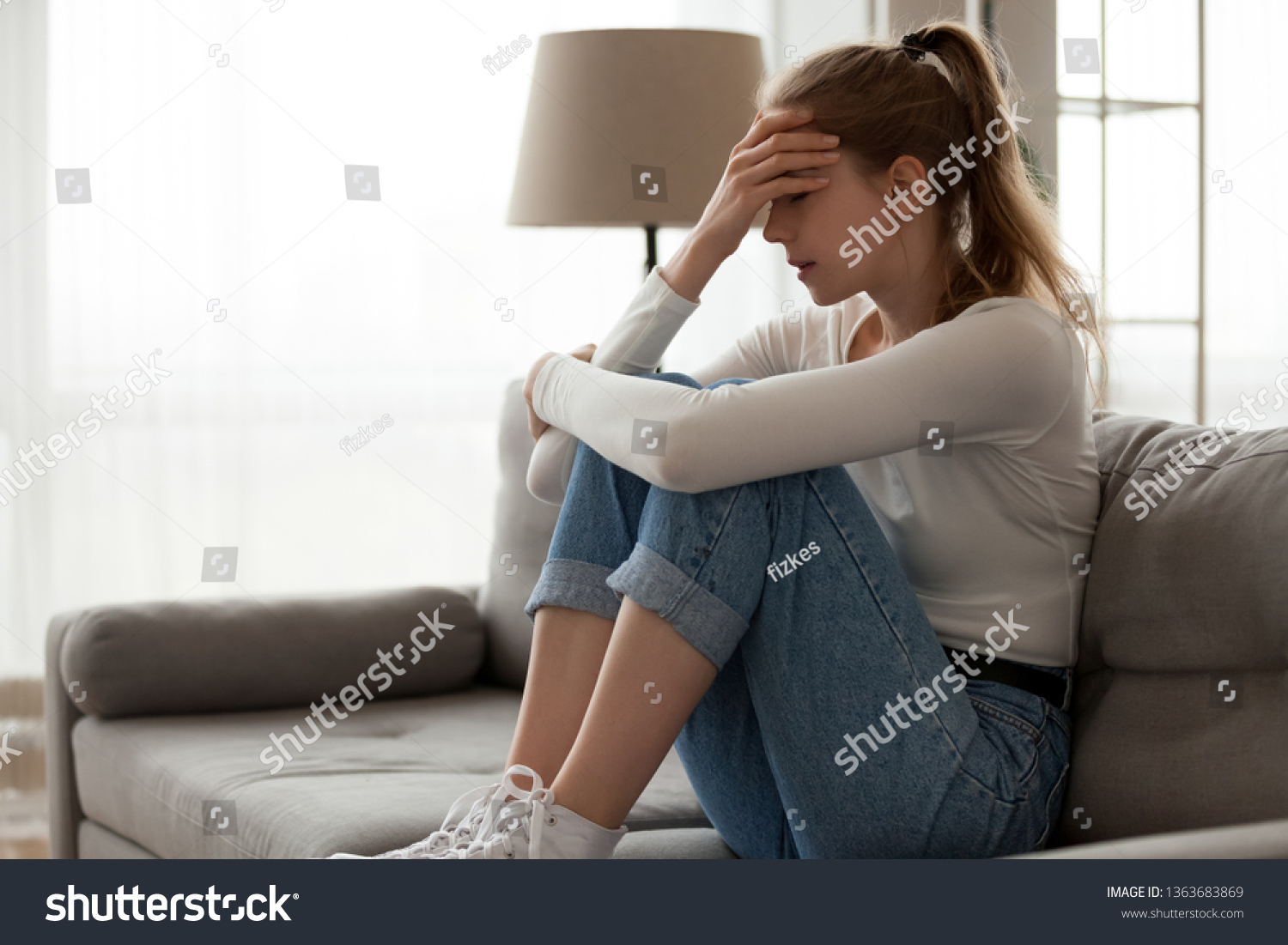 Upset woman frustrated by problem with work or relationships, sitting on couch, embracing knees, covered face in hand, feeling despair and anxiety, loneliness, having psychological trouble #1363683869
