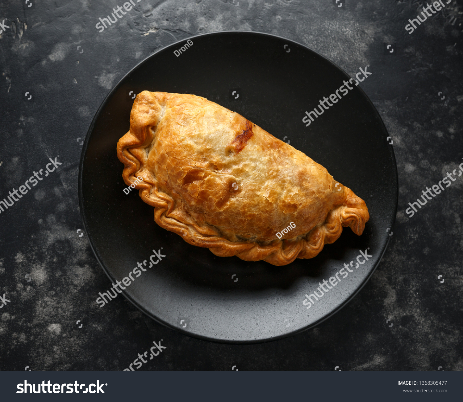 Traditional Cornish pasty filled with beef meat, potato and vegetables on black plate #1368305477