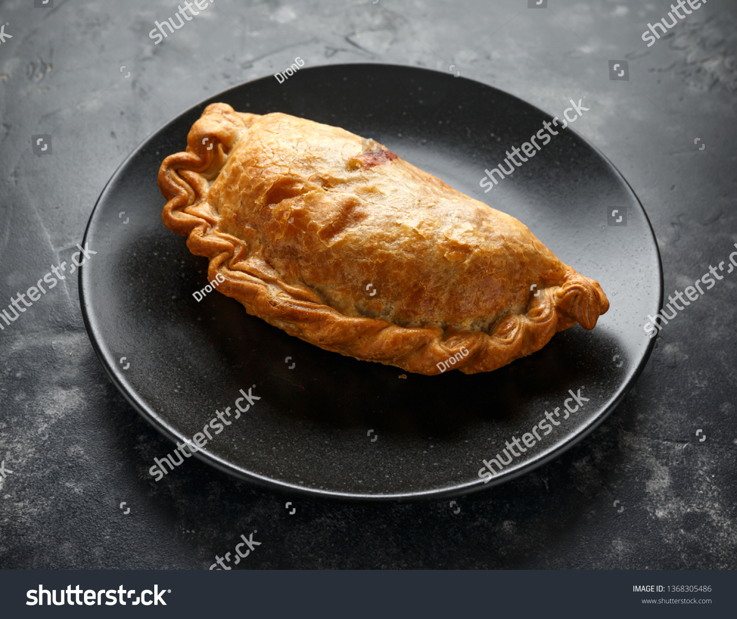 Traditional Cornish pasty filled with beef meat, potato and vegetables on black plate #1368305486