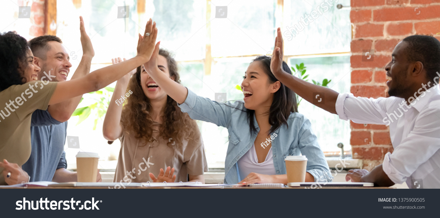 Wide horizontal image multicultural cheerful businesspeople sitting together at meeting giving high five gesture feels excited happy, showing team spirit, celebrating victory goal achievement concept #1375900505
