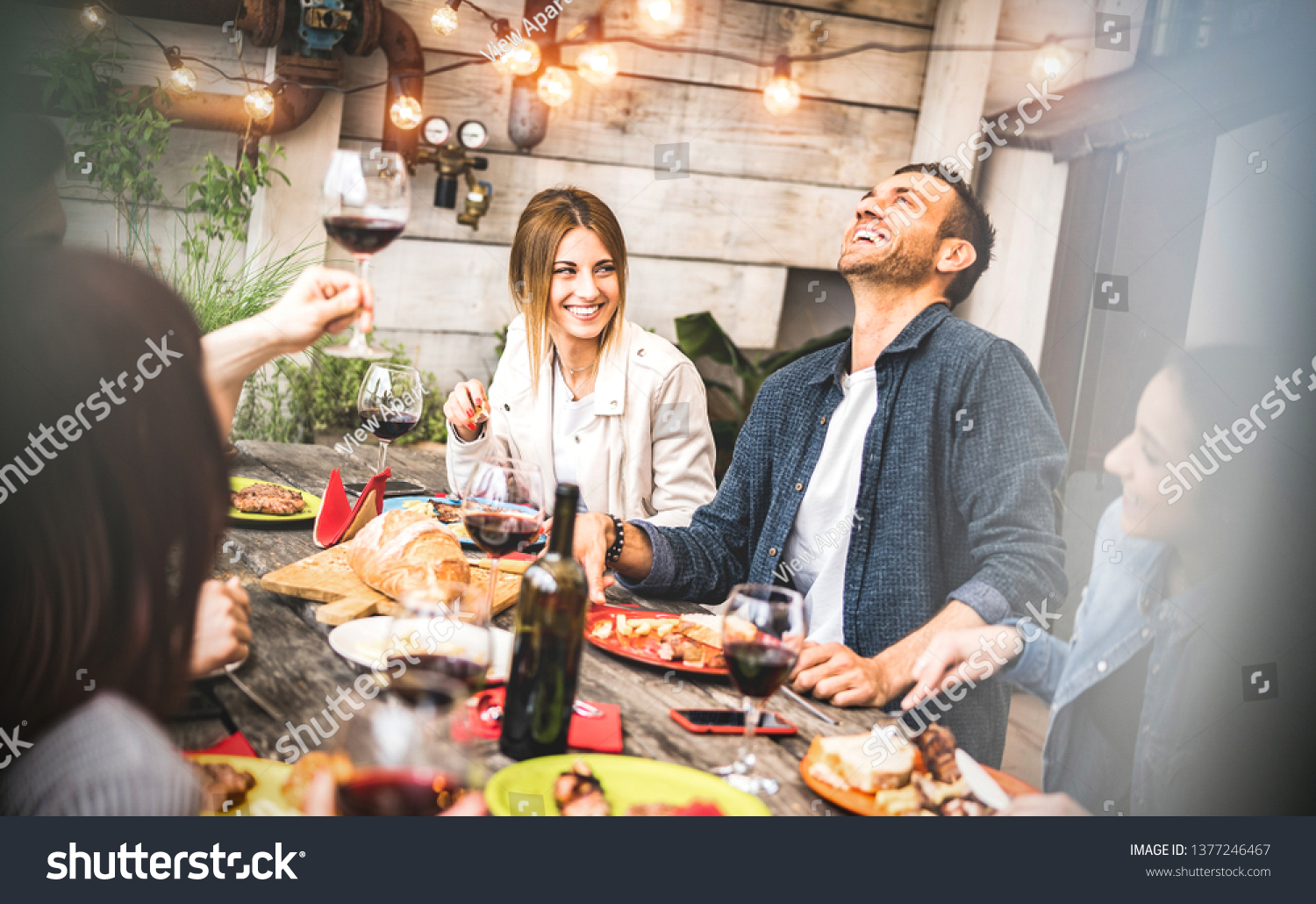 Young friends having fun drinking red wine on balcony at house dinner pic nic party - Hipster millennial people eating bbq food at fancy restaurant together - Dinning life style concept on warm filter #1377246467
