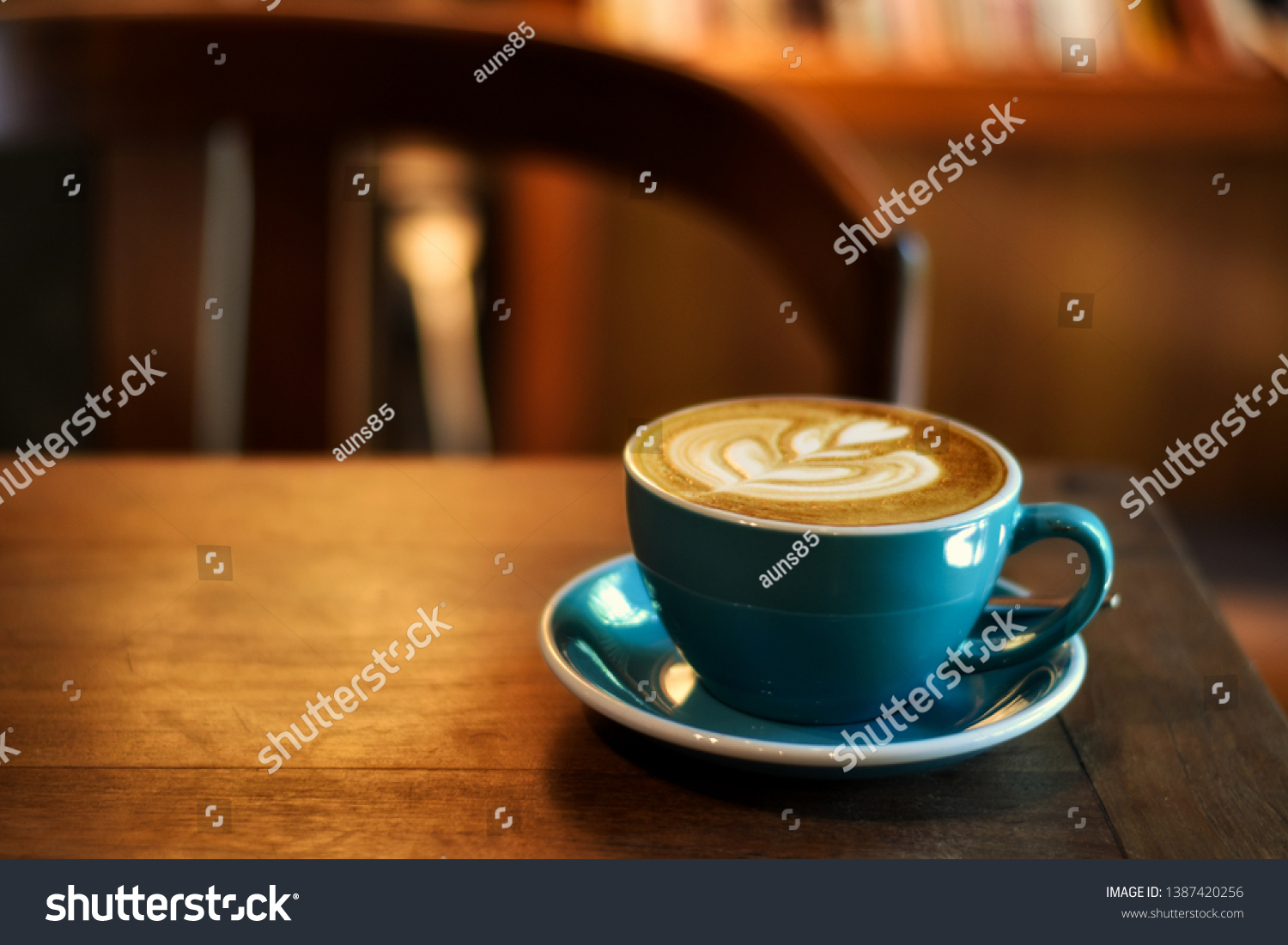 Coffee in blue cup on wooden table in cafe with lighting background #1387420256