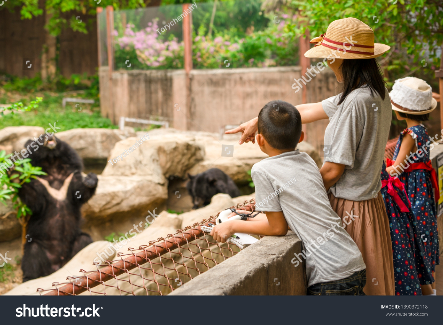 Asian family kids learning outdoor on vacation summer holiday, mother brother and sisters looking bear show for feeding in zoo, boy child holding telescope , pen and notebook for writing knowledge  #1390372118