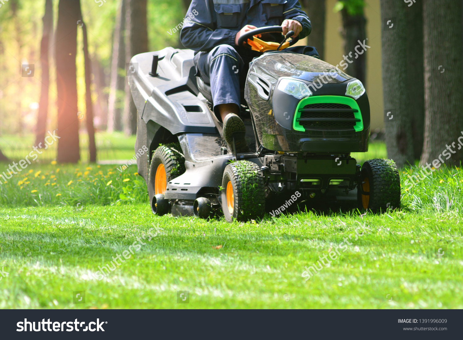 Professional lawn mower with worker cutting the grass in a garden #1391996009