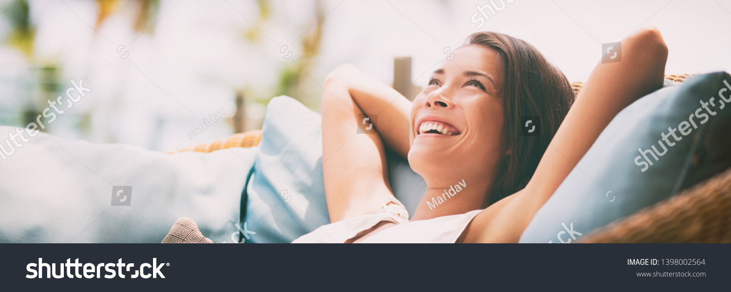 Relaxing home lifestyle happy woman in relax luxury hotel room sofa lying back with arms behind head smiling. Asian girl in comfortable lounging chair travel living. #1398002564