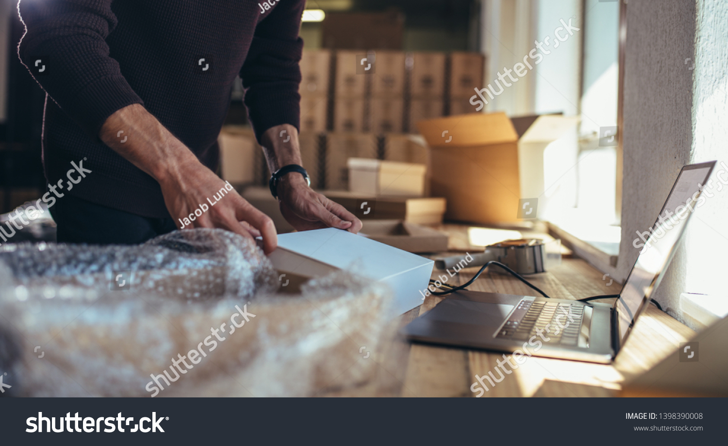 Small business owner packing in the cardbox at workplace. Cropped shot of man preparing a parcel for delivery at online selling business office. #1398390008