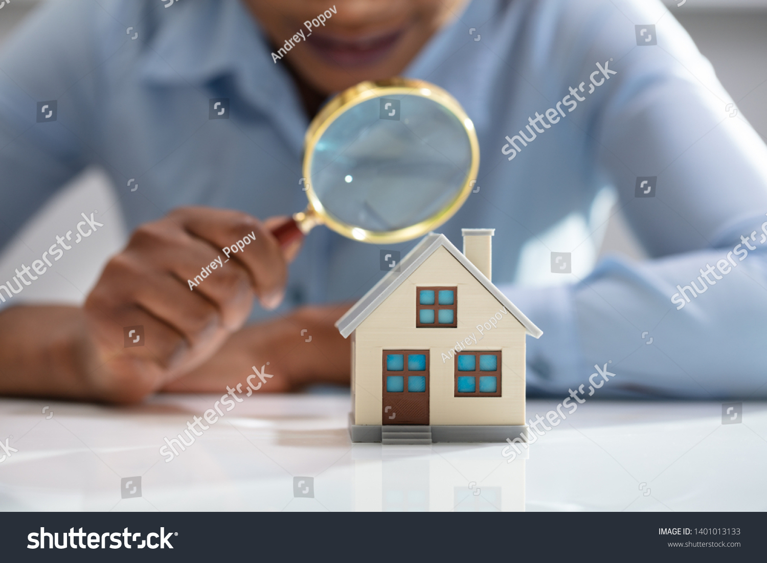 Close-up Of A Businesswoman's Hand Holding Magnifying Glass Over House Model Over Desk #1401013133
