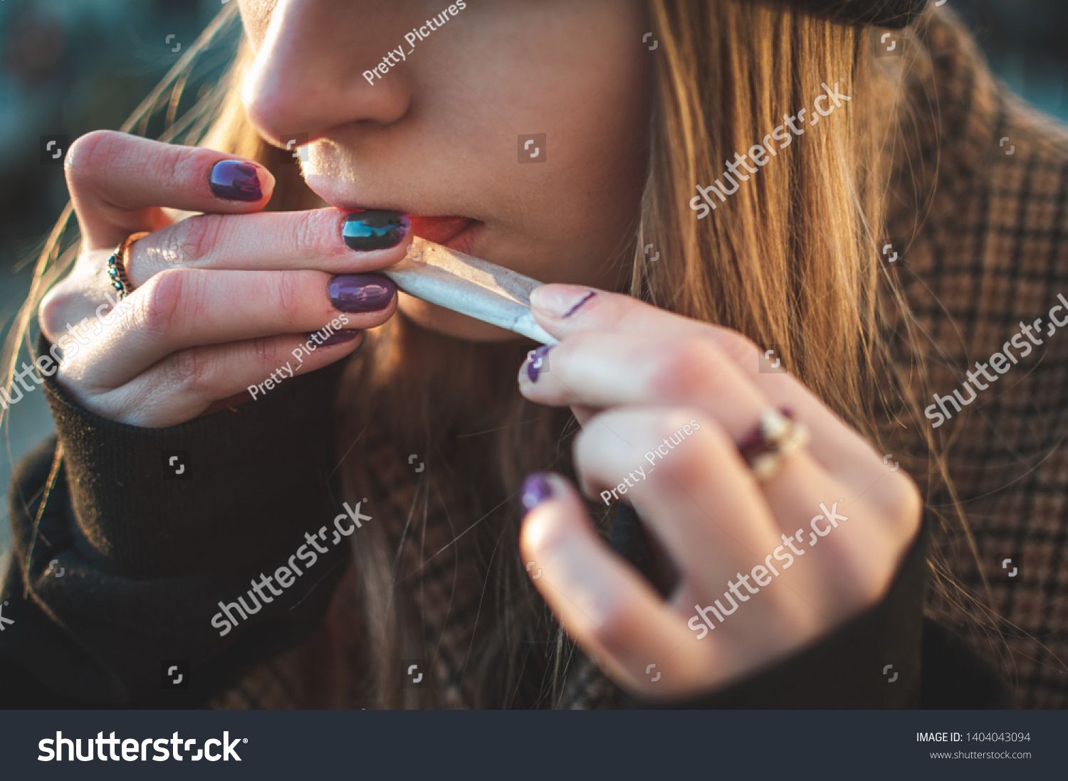 Close up picture of a young lady rolling a Tabasco cigarette by her self. Making a Rollie. Bad habits, lung problems. Sunny weather, sitting outside, serious and Moodie picture. warm desaturated color #1404043094