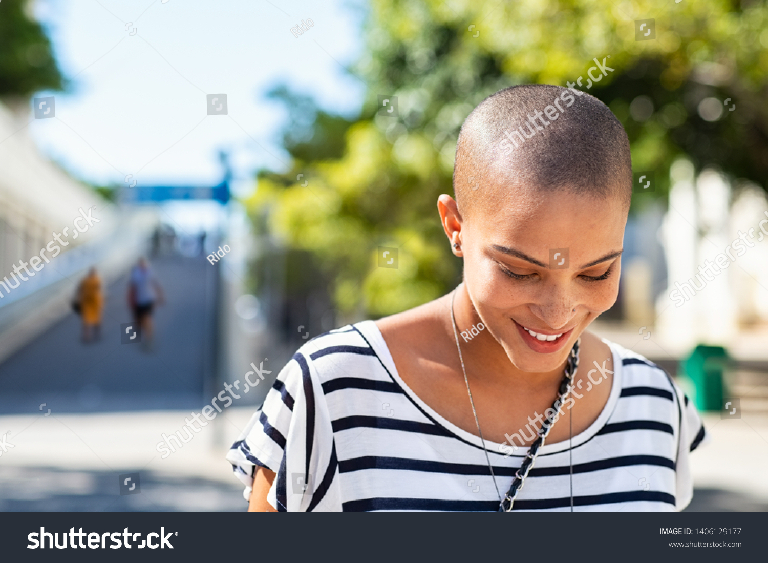 Portrait of happy and young bald woman smiling. Carefree trendy girl with bald head after cancer chemotherapy treatment. Stylish and beautiful woman feeling free in a city street. #1406129177