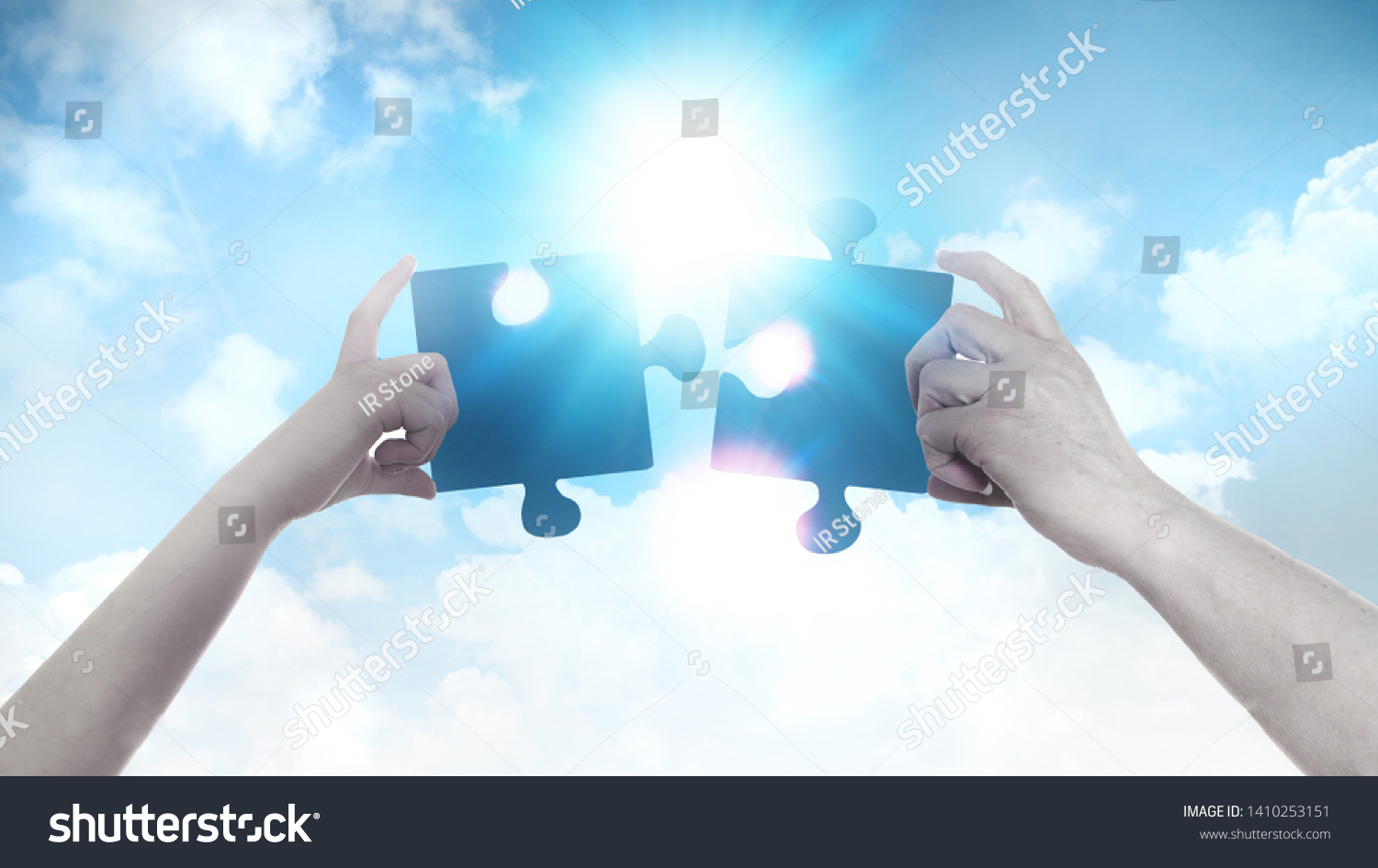 Two hands holding a puzzle pieces agains of blue sky background and sun. Business, support, finding the right decision concept.  #1410253151