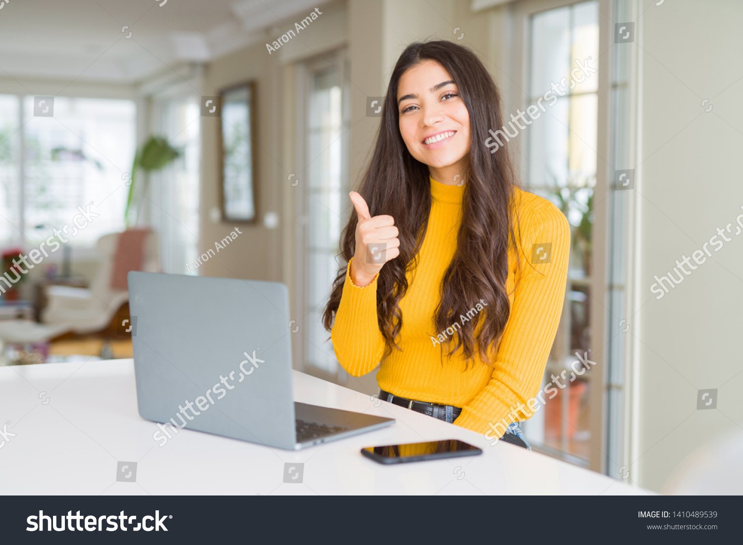 Young woman using computer laptop doing happy thumbs up gesture with hand. Approving expression looking at the camera with showing success. #1410489539