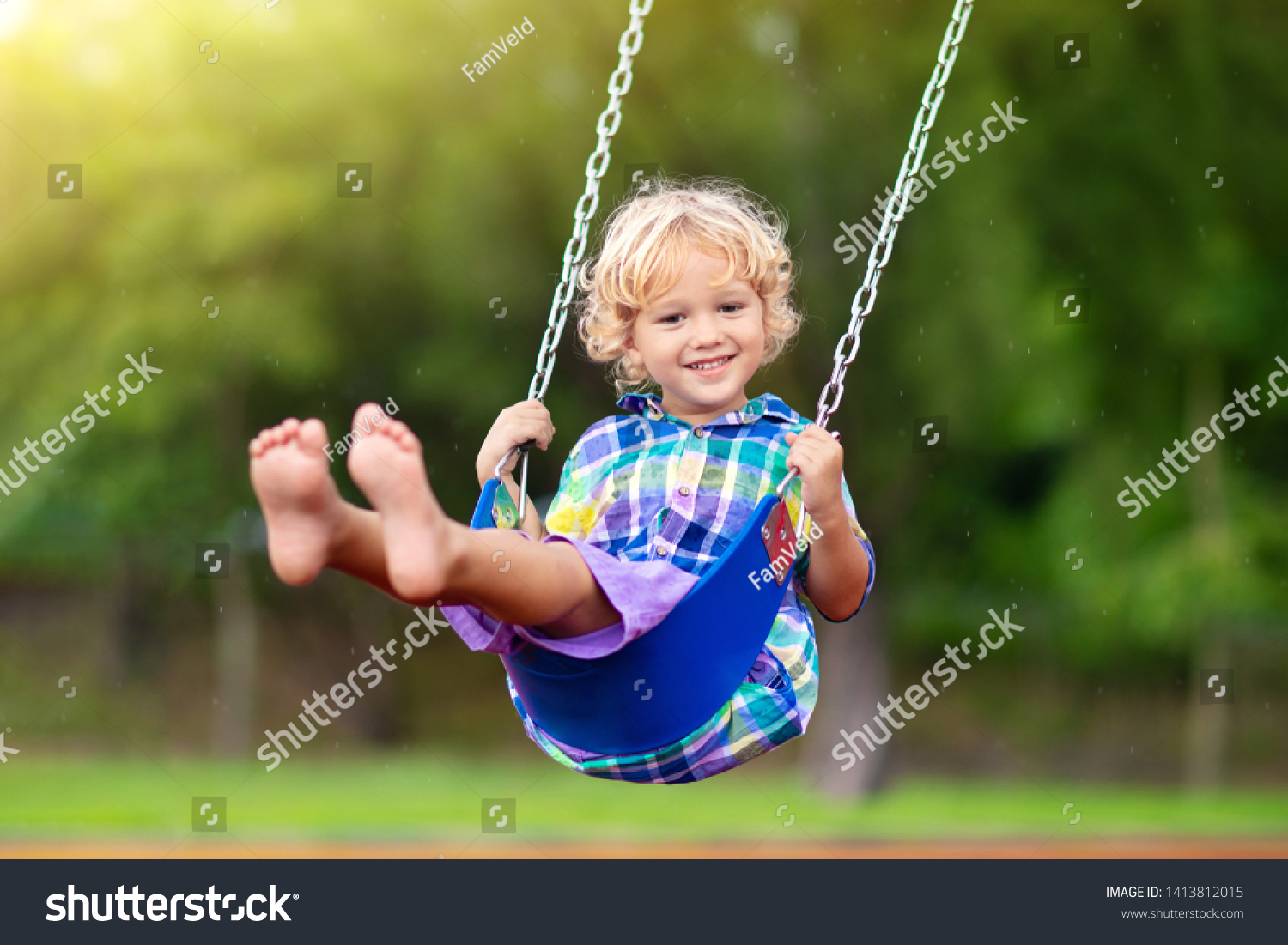 Child playing on outdoor playground in rain. Kids play on school or kindergarten yard. Active kid on colorful swing. Healthy summer activity for children in rainy weather. Little boy swinging. #1413812015