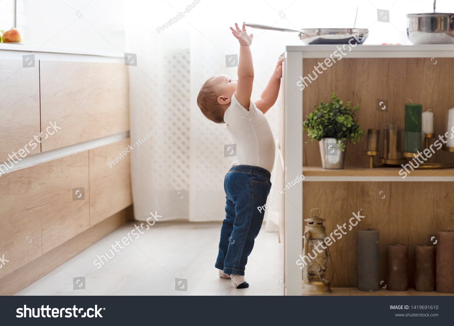 Child safety at home concept. Little baby reaching for hot pan on stove in kitchen, empty space #1419691610