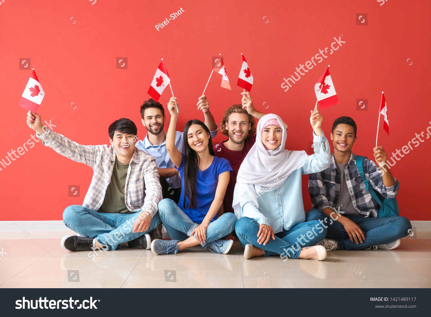 Group of students with Canadian flags sitting near color wall #1421489117
