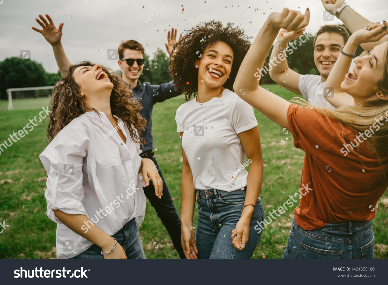 Group of five friends having fun at the park - Millennials dancing in a meadow among confetti thrown in the air - Day of freedom and carefree #1421555180
