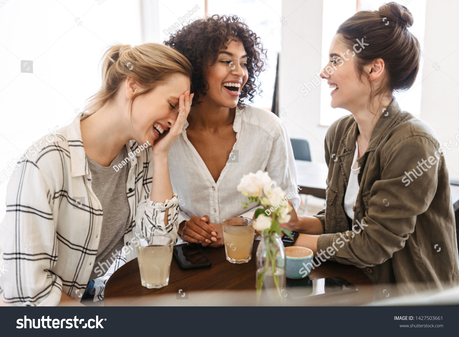 Happy young women friends having coffee break while relaxing at the cafe indoors #1427503661