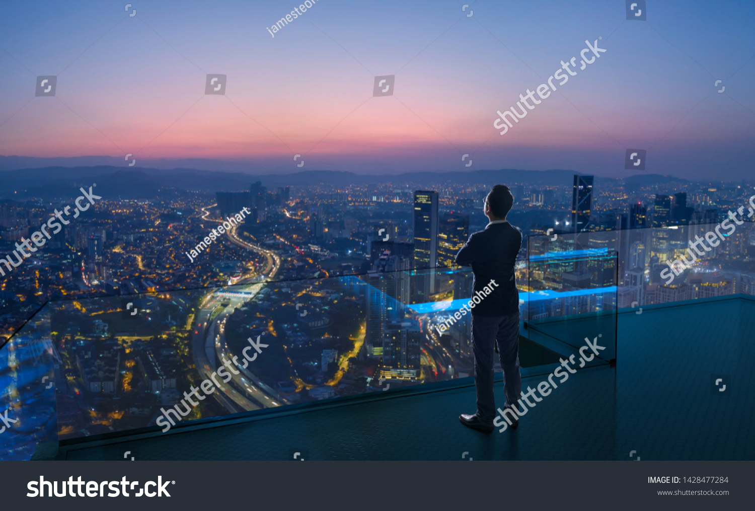 Businessman standing on open roof top balcony watching city night view . Business ambition and vision concept . #1428477284