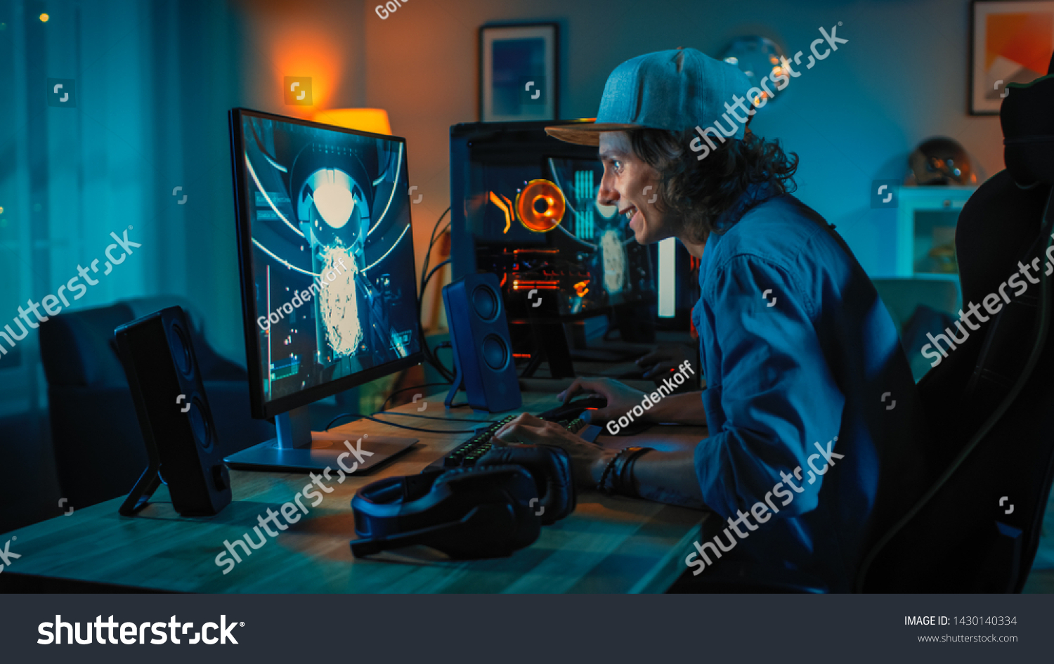 Professional Gamer Playing First-Person Shooter Online Video Game on His Powerful Personal Computer. Room and PC have Colorful Neon Led Lights. Young Man is Wearing a Cap. Cozy Evening at Home. #1430140334