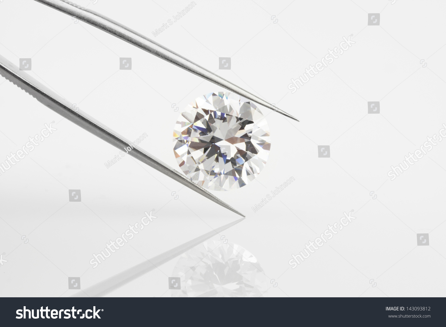 Diamond held within tweezers. Large round diamond, angled and reflected on pale background. #143093812