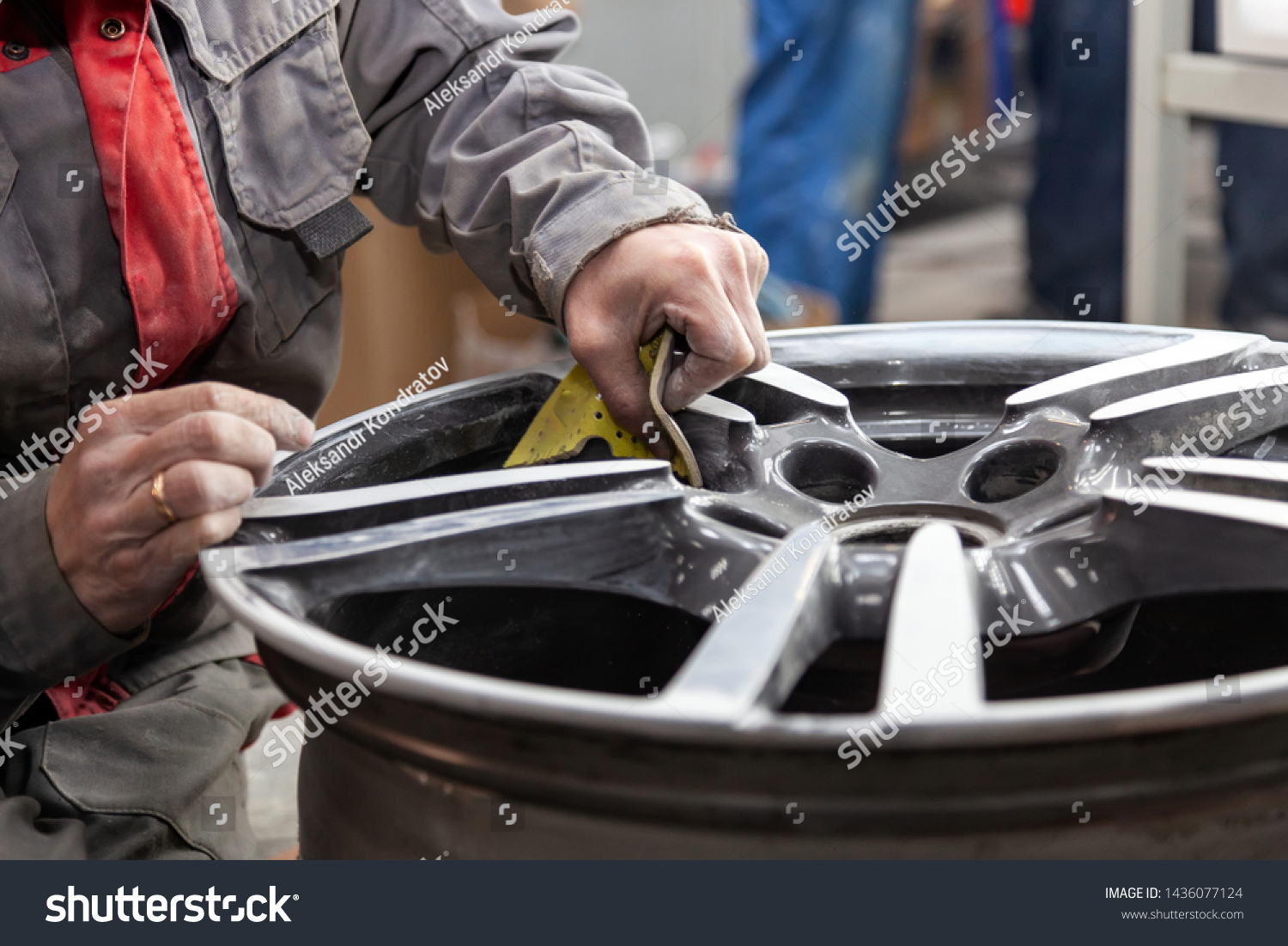 Master body repair man is working on preparing the surface of the aluminum wheel of the car for subsequent painting in the workshop, cleaning and leveling the disk with the help of abrasive material #1436077124