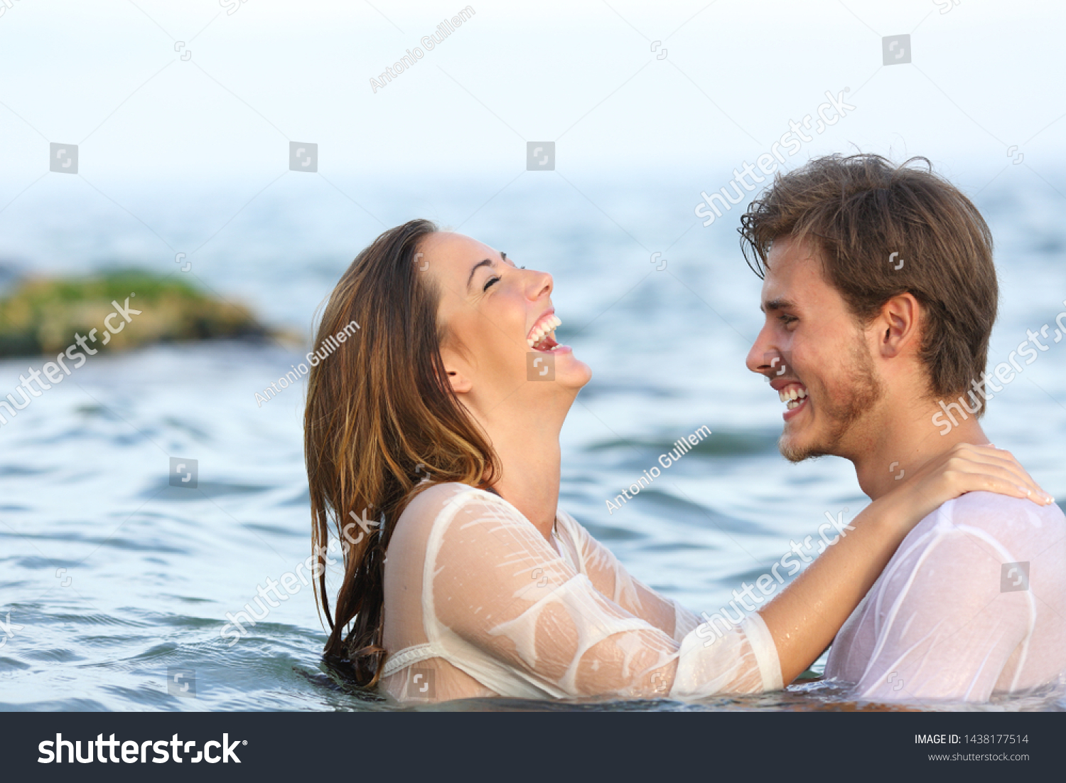Side view portrait of a happy spontaneous couple joking in the water on the beach #1438177514
