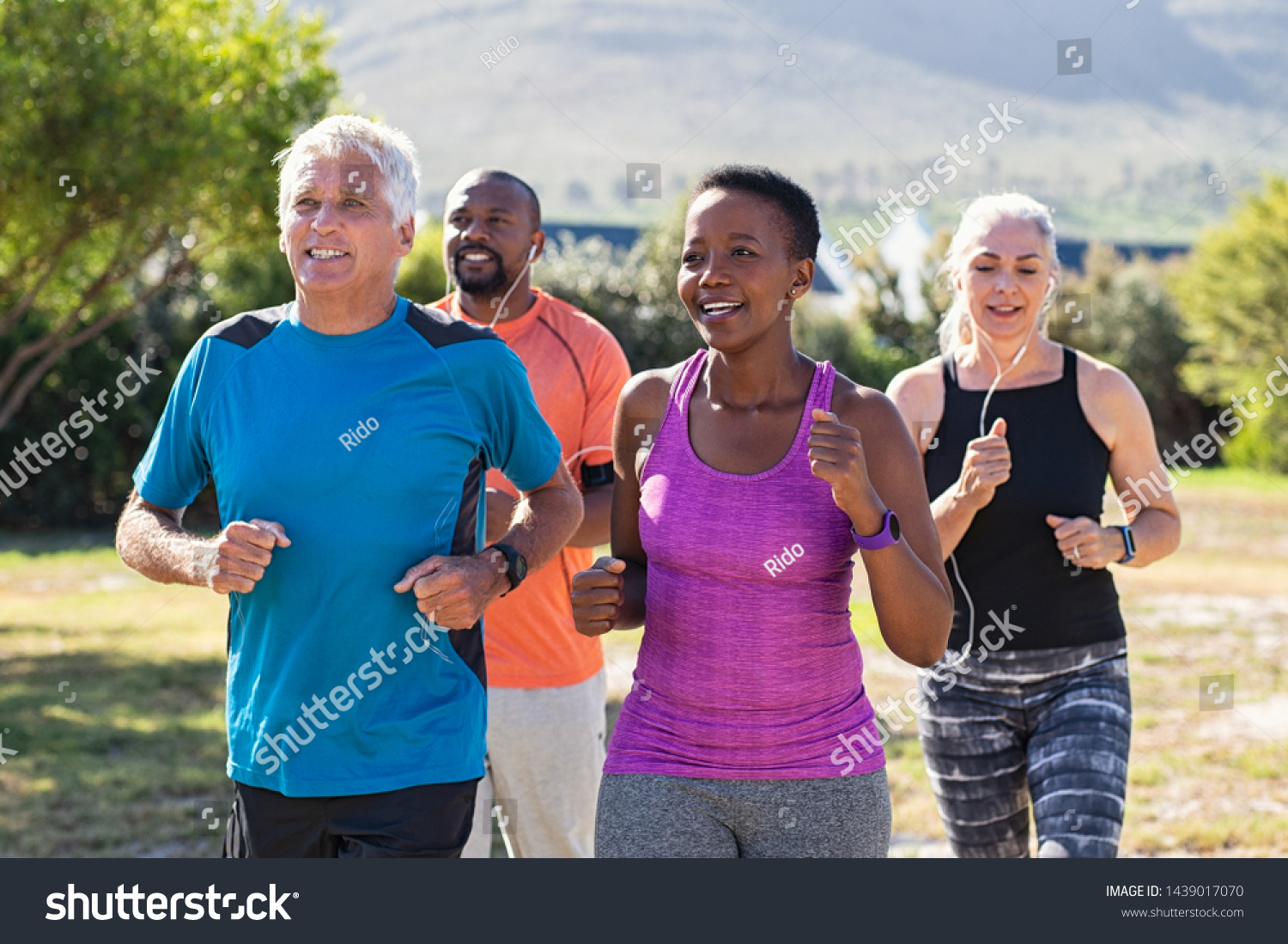 Healthy group of mature people jogging on track at park. Happy senior couple running at park with african friends. Multiethnic middle aged friends exercising together outdoor. #1439017070