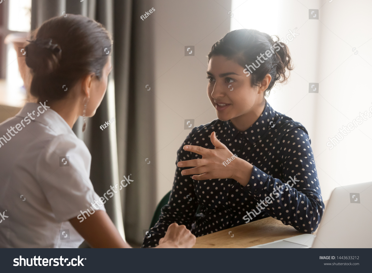 Serious indian mentor teacher worker talk to female colleague teach intern discussing new skills learning sit at work desk, two diverse coworkers work together help cooperate on project in teamwork #1443633212