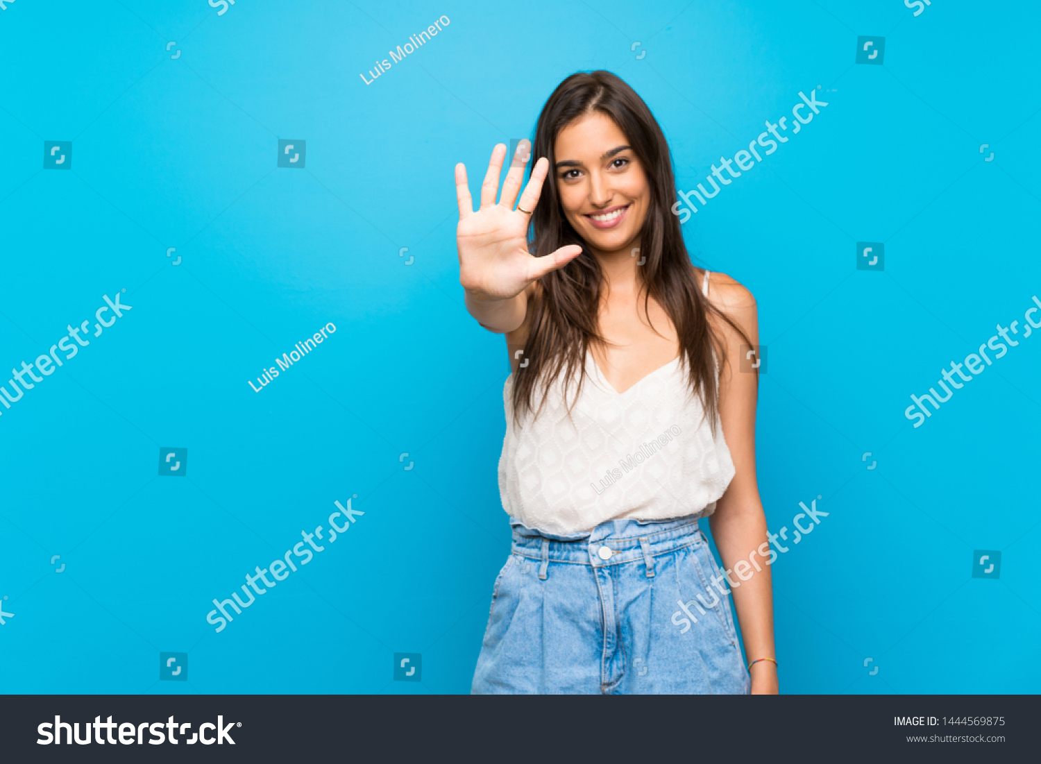 Young woman over isolated blue background counting five with fingers #1444569875
