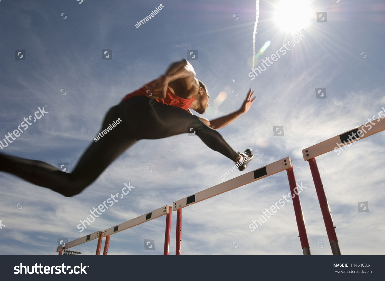 Low angle view of a male athlete jumping hurdle against the sky #144640304