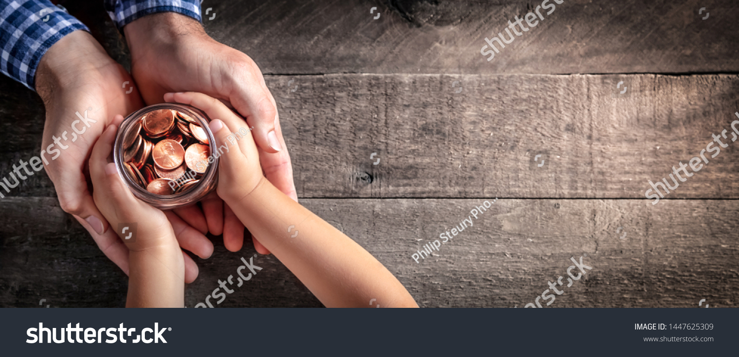 Hands Of Father Giving Jar Of Coins To Child On Wooden Table Background - Inheritance / Parent Providing For Children Concept #1447625309