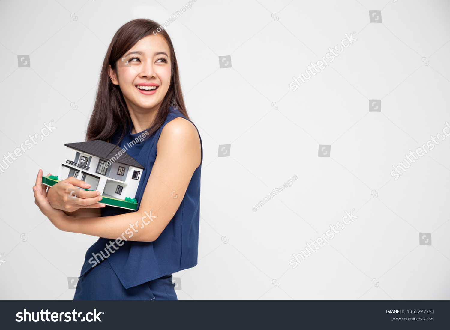 Young Asian woman smiling and hugging dream house sample model isolated over white background, Real estate and home insurance concept #1452287384