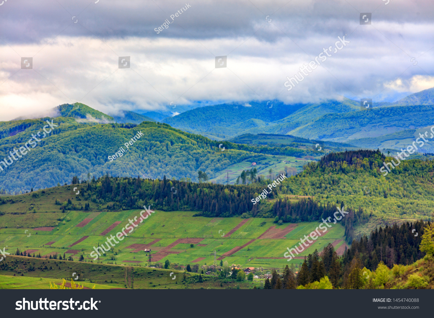 In the valley on the mountainside stretched rectangular agricultural land plots against the backdrop of the picturesque landscape of the Carpathian Mountains, shrouded in mist. #1454740088
