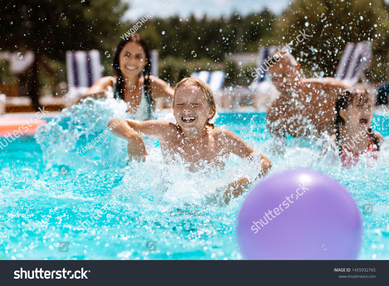 Ball in pool. Cheerful happy parents and children laughing while playing ball in swimming pool #1455932765