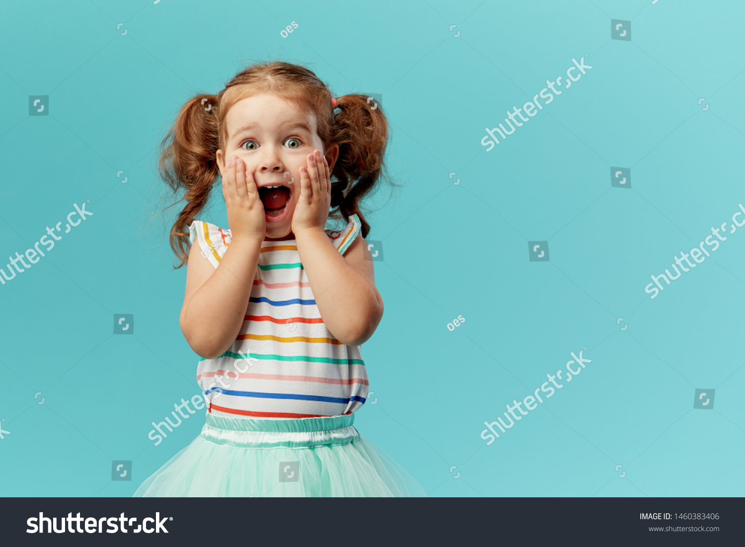 Portrait of surprised cute little toddler girl child standing isolated over blue background. Looking at camera. hands near open mouth #1460383406