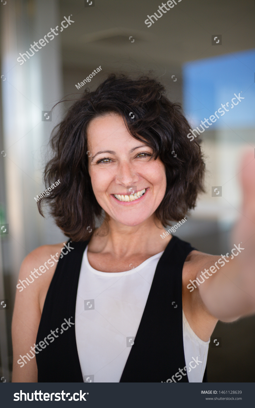 Selfie of happy joyful curly haired woman in casual. Excited middle aged lady holding smartphone and taking picture of herself. Happy woman portrait concept #1461128639