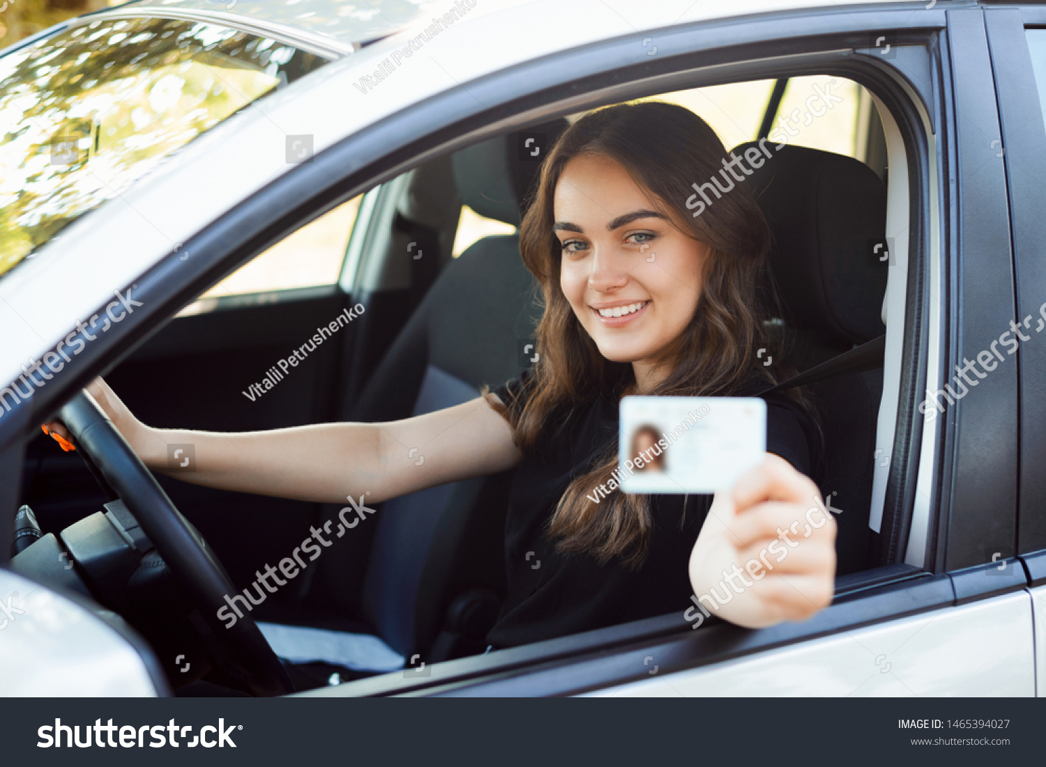 Happy student driver sitting in the modern silver car and showing driving car license to the camera having good mood and happy to pass driving exams #1465394027