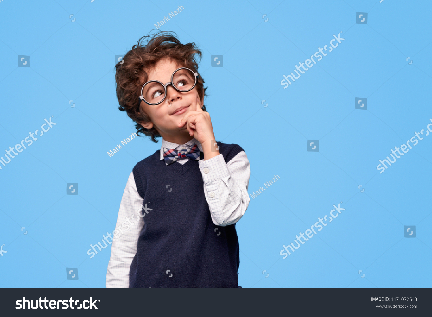 Smart wunderkind in nerdy glasses and school uniform touching cheek and looking up while thinking against blue background #1471072643